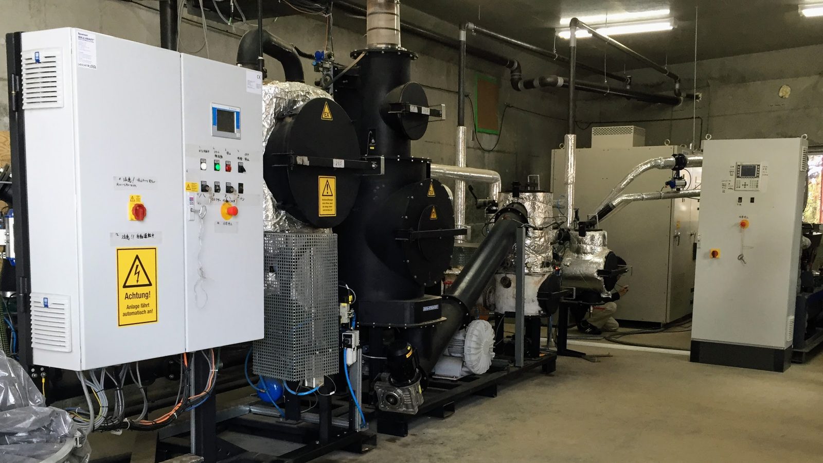 福島県郡山市湖南町の江湖村に設置されたSpanner製45kW木質バイオマスガス化CHP設備の全景。左に制御盤、中央にガス化炉、右奥に発電機ユニットが並ぶ。
